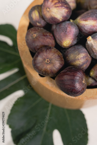 A wooden bowl full of ripe figs with green leaves photo