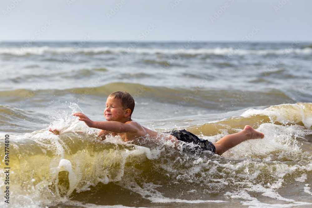 Fototapeta premium Young cheerful boy having fun at sea waves.