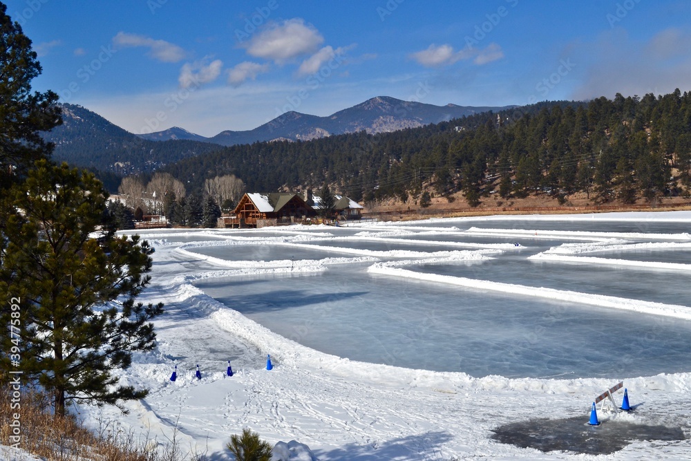 Ice skating on Evergreen Lake with a mountain view, blue sky and pines. Winter recreational scene in Colorado mountains.
