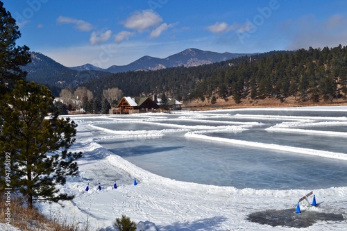 Ice skating on Evergreen Lake with a mountain view, blue sky and pines. Winter recreational scene in Colorado mountains.
