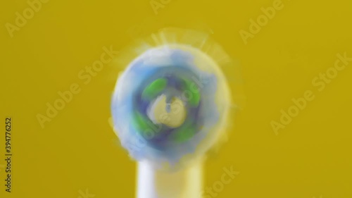 super close-up of electric toothbrush bristles, brush turns on and bristles rotate isolated on yellow background