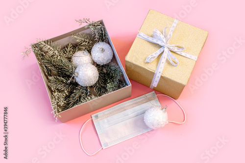 Gift box with white balls, medical protective mask and branches of christmas tree on pink background. Christmas and New Year during pandemic of coronavirus infection. Flat lay, top view .