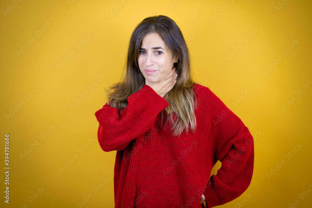 Young beautiful woman wearing red sweater over isolated yellow background touching painful neck, sore throat for flu, clod and infection Young beautiful woman wearing red sweater over isolated yellow background touching painful neck, sore throat for flu, clod and infection
