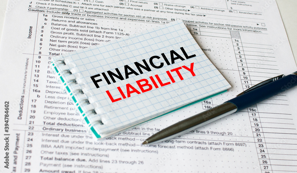 Notepad with text Financial Liability lying on financial tables with a pen Notepad with text Financial Liability lying on financial tables with a pen