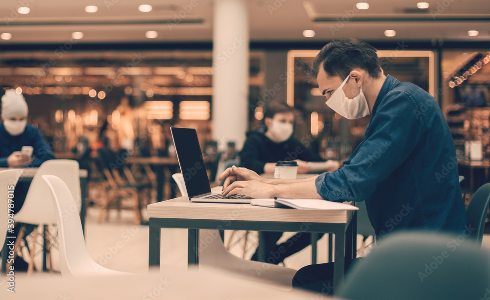 image of people in protective masks using laptops in a food court.