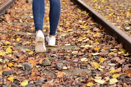 Walking legs wearing blue jeans and white shoes on autumn leaves