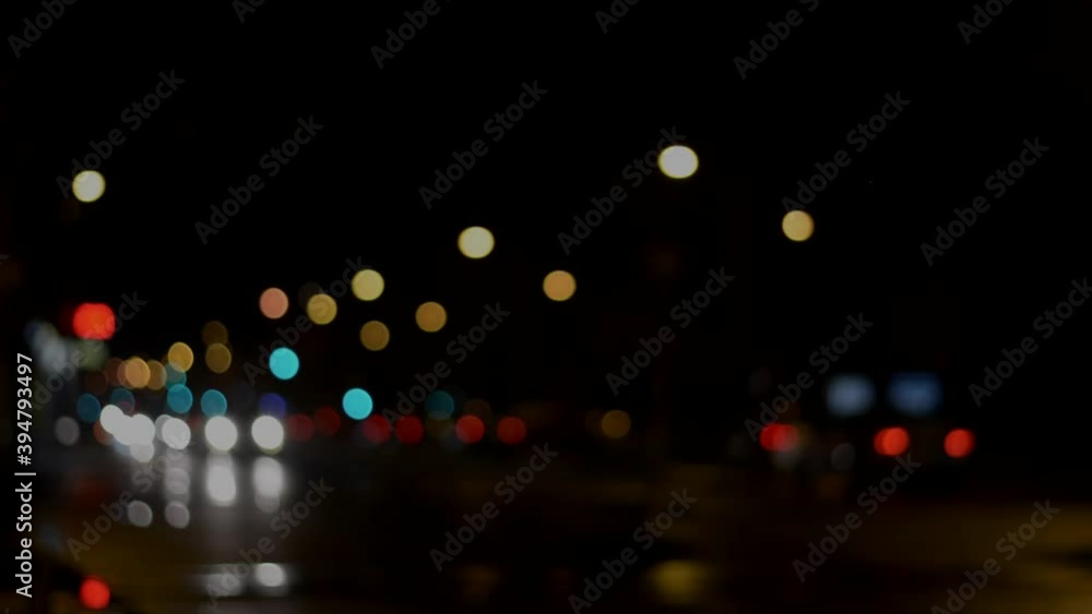 glittering, cinematic bokeh in dark blurry background at night. The round colorful bokeh shine from car lights in traffic on a wet city street. 