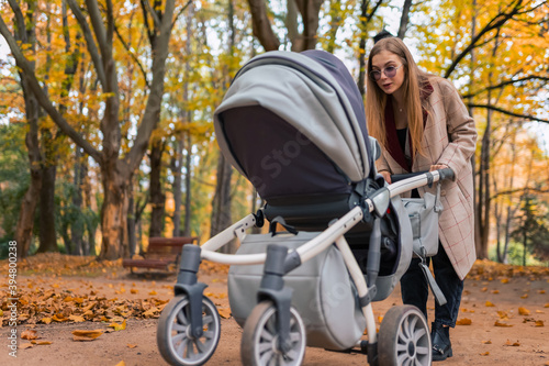 Cheerful mom playing with newborn baby in stroller. Woman walking in the park with pram