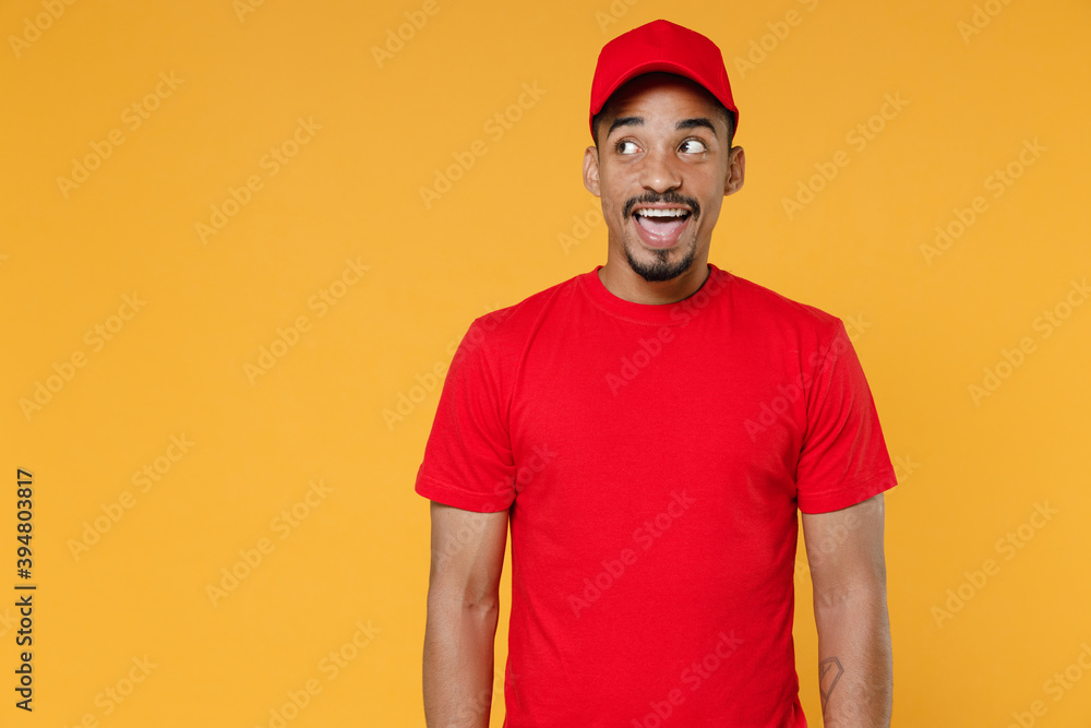Delivery employee african man 20s in red cap blank print t-shirt uniform workwear work courier dealer service during quarantine coronavirus covid-19 virus concept isolated on yellow background studio. Delivery employee african man 20s in red cap blank print t-shirt uniform workwear work courier dealer service during quarantine coronavirus covid-19 virus concept isolated on yellow background studio.
