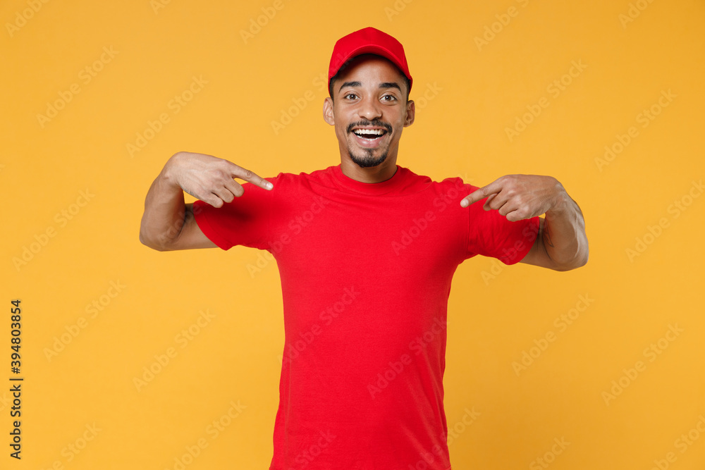 Naklejka premium Delivery employee african man 20s in red cap blank print t-shirt uniform workwear work courier dealer service during quarantine coronavirus covid-19 virus concept isolated on yellow background studio.