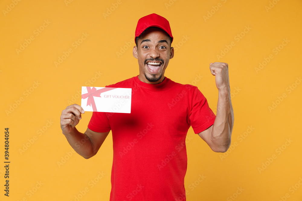 Delivery employee african man 20s in red cap blank print t-shirt uniform workwear work courier dealer service concept hold mockup gift certificate voucher coupon isolated on yellow background studio. Delivery employee african man 20s in red cap blank print t-shirt uniform workwear work courier dealer service concept hold mockup gift certificate voucher coupon isolated on yellow background studio.