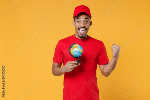 Delivery employee african man in red cap blank t-shirt uniform workwear work courier service during quarantine coronavirus covid-19 virus concept hold world globe isolated on yellow background studio.