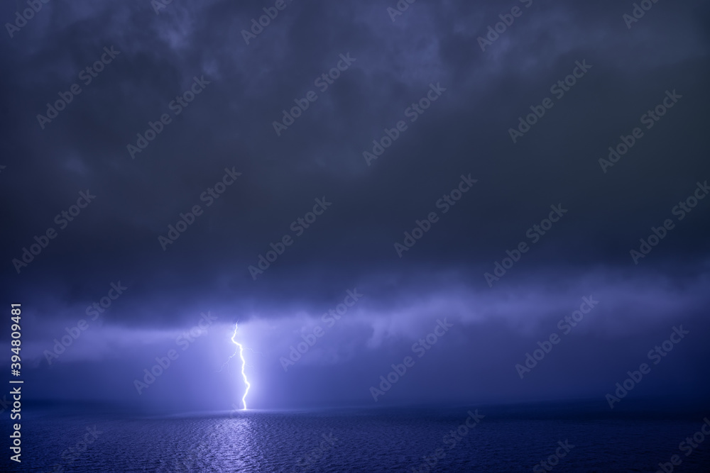 Single linear lightning over the sea with reflection under dark clouds