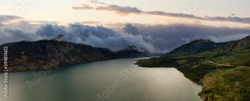 Beautiful Panoramic View of Lake alongside Scenic Road surrounded by Mountains and Trees on a Cloudy Day. Aerial Drone Shot. Taken near Klondike Highway, Southern Yukon, Canada.