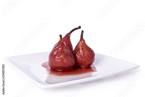 Fresh Dutch poached Pears (stoofpeertjes: Gieser Wildeman) in red wine with cinnamon and clove,  on white plate. Glazed fruit, isolated an a white background.