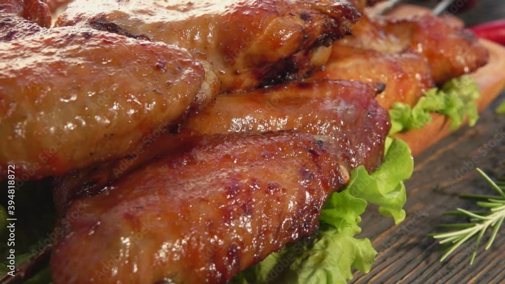 Close-up of delicious fried chicken wings on the skewers on the wooden plate with green salad leaves Close-up of delicious fried chicken wings on the skewers on the wooden plate with green salad leaves