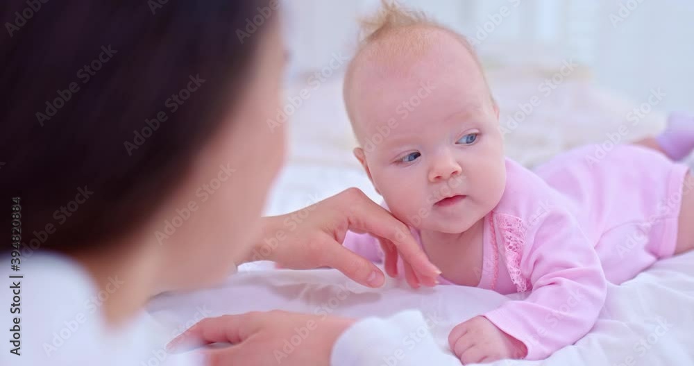 Portrait, a newborn little girl with big blue eyes lies on her tummy on a light bed and smiles at her mother. Mom strokes the baby on the cheeks, the baby learns to hold her head. 4k, ProRes Portrait, a newborn little girl with big blue eyes lies on her tummy on a light bed and smiles at her mother. Mom strokes the baby on the cheeks, the baby learns to hold her head. 4k, ProRes