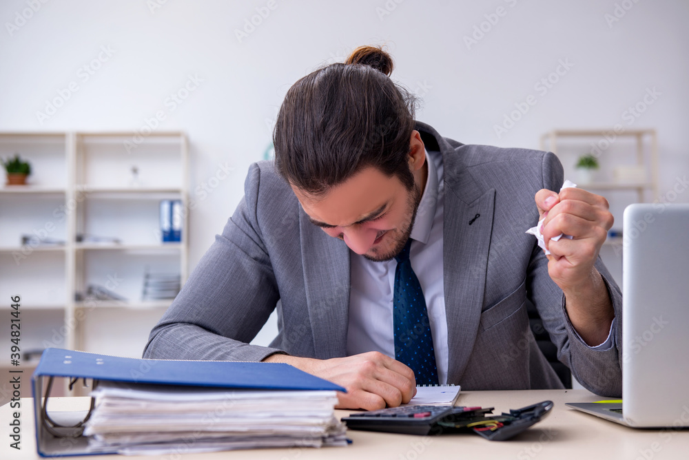 Young male employee unhappy with excessive work in the office Young male employee unhappy with excessive work in the office