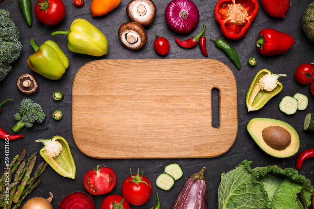 Wooden board and fresh vegetables on black table, flat lay. Space for text Wooden board and fresh vegetables on black table, flat lay. Space for text