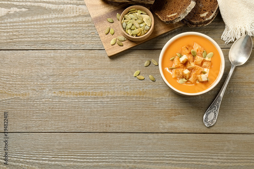 Tasty creamy pumpkin soup served with bread and seeds on wooden table, flat lay. Space for text