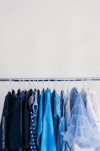 Fast fashion, Sustainable fashion, minimalist wardrobe. Variety of female blue clothing on hanging on white background with copy space. Fashion minimal style banner