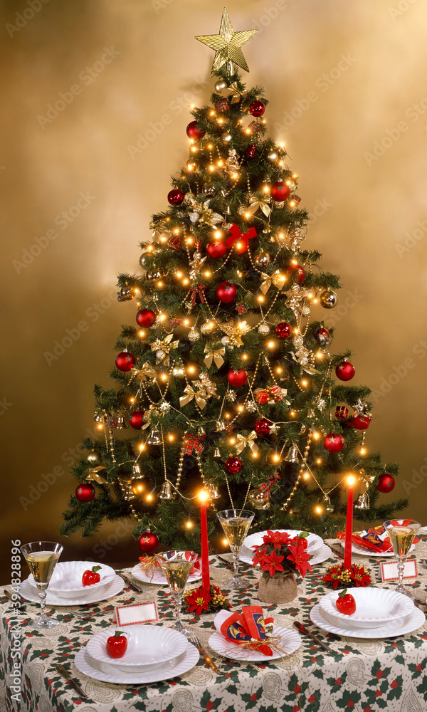 A beautiful decorated Christmas tree next to a laid table and a golden background A beautiful decorated Christmas tree next to a laid table and a golden background