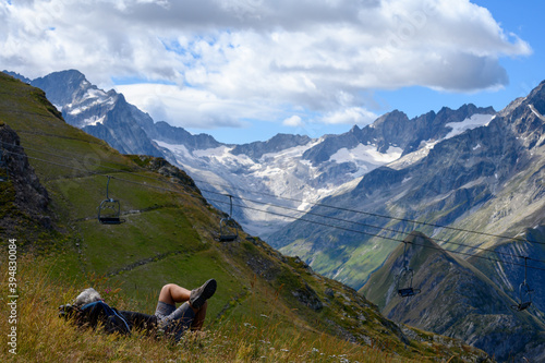 Hiker resting on grass near ski station Les deux Alpes and view on Alpine mountains peaks in summer, Isere, France