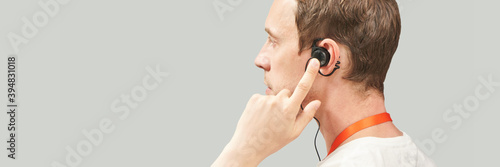 Men in call center. White t-shirt. Headset for telemarketing. Male manager helps customer. Phone operator. Studio portrait. Person multi language translator. Grey background. Earphones