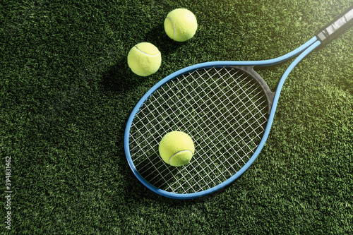 Tennis racket and balls on green grass, flat lay. Sports equipment
