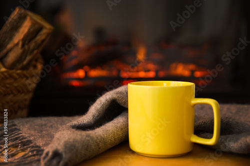 Cup with hot drink and blanket against fireplace
