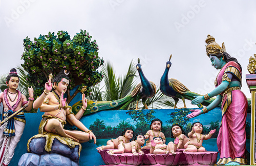 Kadirampura, Karnataka, India - November 4, 2013: Sri Murugan Temple. Colorful statues representing Parvati presenting to Shiva 6 babies that will become Muruga under silver sky. Peacocks present. photo