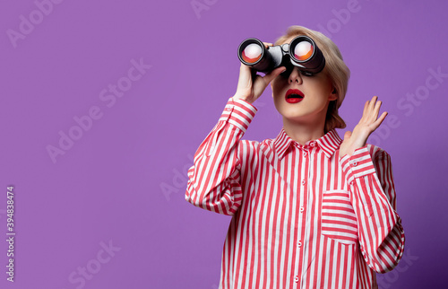 Beautiful woman in red striped shirt with binocular on purple background