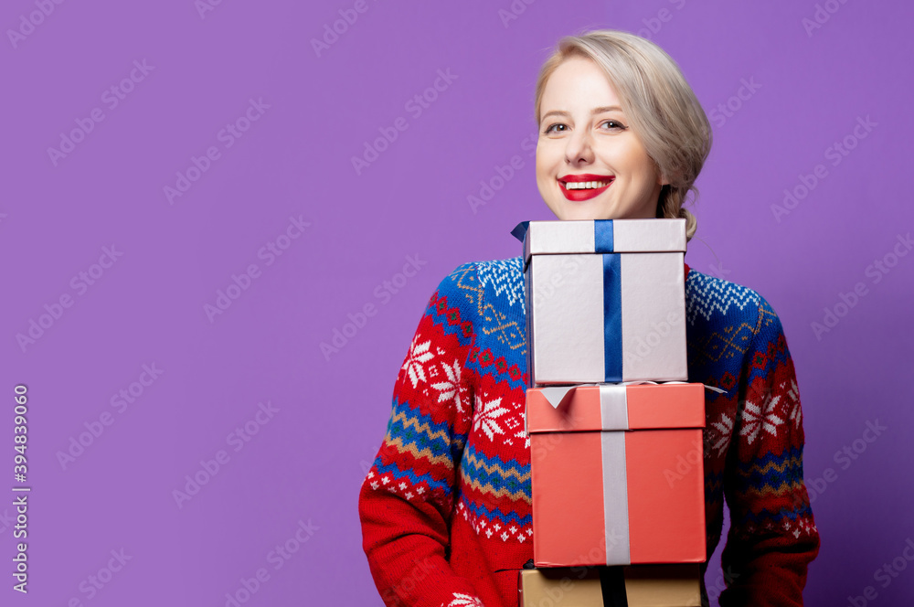 Beautiful woman in Christmas sweater with gift box on purple background Beautiful woman in Christmas sweater with gift box on purple background