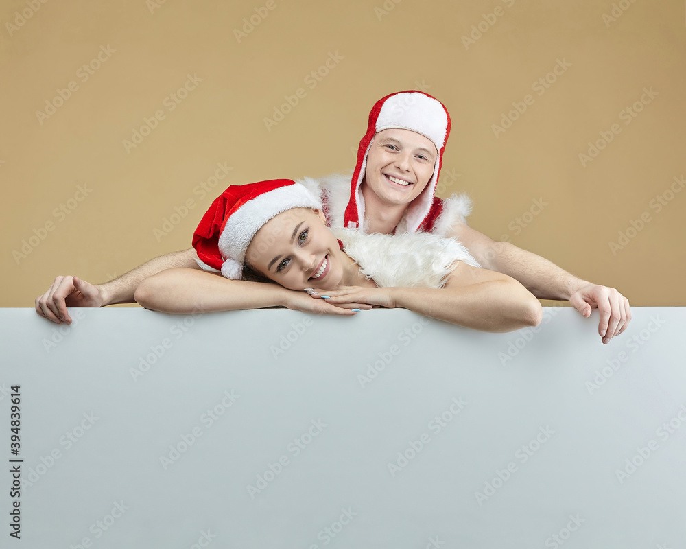 Obraz premium young guy and a girl in Santa Claus costumes on an advertising layout. Christmas and New year concept