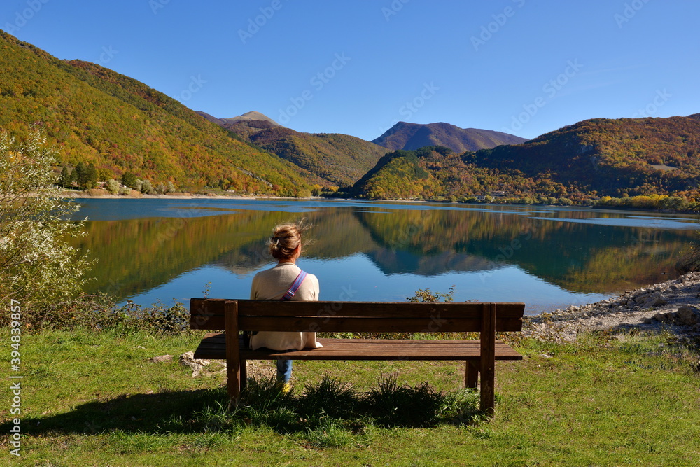 Woman relaxing on a bench in front of lake and mountain