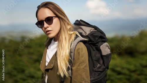Portrait of adorable beautiful  girl, wearing casual white t-shirt and jacket with a backpack, wandering, exploring the world. Spending spare time in the mountain. Hiker is enjoying a wonderful moment