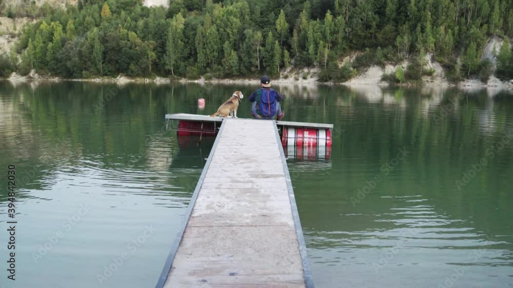 4K Man with beagle sitting on wooden pier contemplating green surface of lake. Seasonal autumn footage, peaceful footage, loneliness and time alone concept. 4K Man with beagle sitting on wooden pier contemplating green surface of lake. Seasonal autumn footage, peaceful footage, loneliness and time alone concept.
