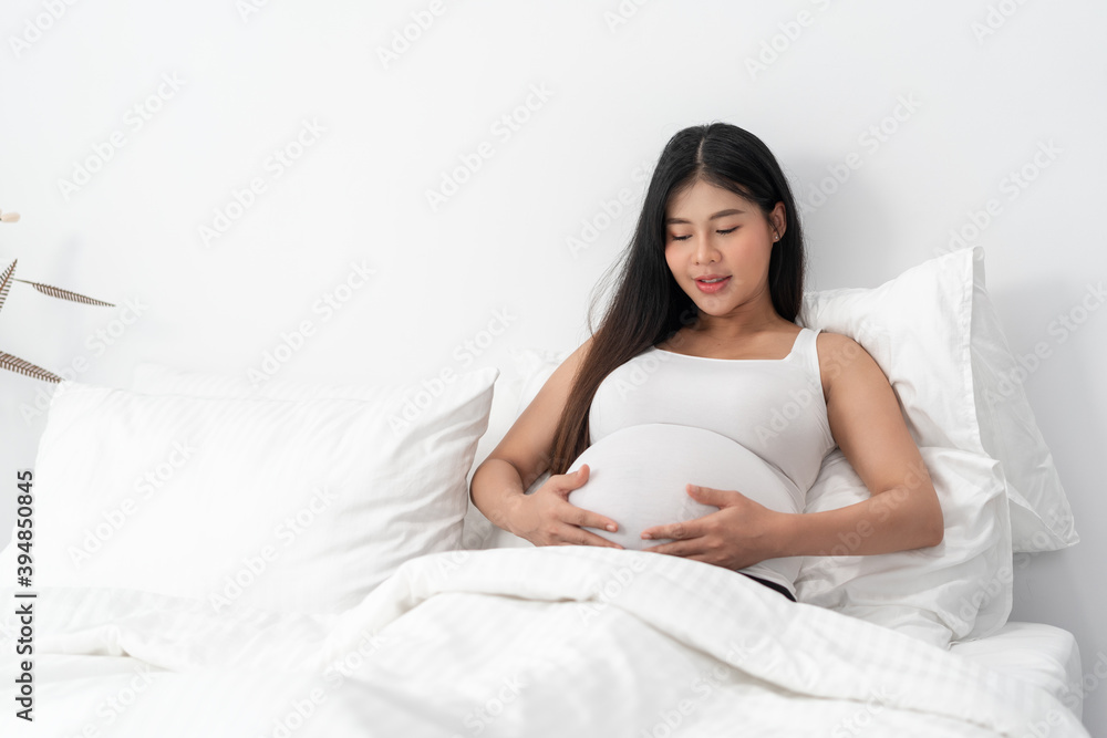 Asia happy pregnant woman is sitting on bed and and touching her belly. pregnancy, motherhood, people and expectation concept Asia happy pregnant woman is sitting on bed and and touching her belly. pregnancy, motherhood, people and expectation concept