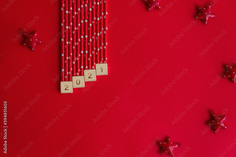 On a red homogeneous isolated background, New Year's tubes lie among the stars. Christmas background for holiday card with lettering numbers 2021. Place for text. Copy space, top view. Layout flatlay