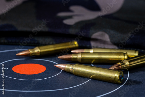 Loose rounds of rifle ammunition scattered on top of a paper target with a camouflage background. Background and foreground blurred with a shallow depth of focus.