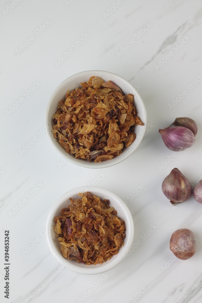 Bawang Merah Goreng or fried shallots, popular Indonesian food topping. Served on white ceramic bowl. Isolated background, copy space. Bawang Merah Goreng or fried shallots, popular Indonesian food topping. Served on white ceramic bowl. Isolated background, copy space.