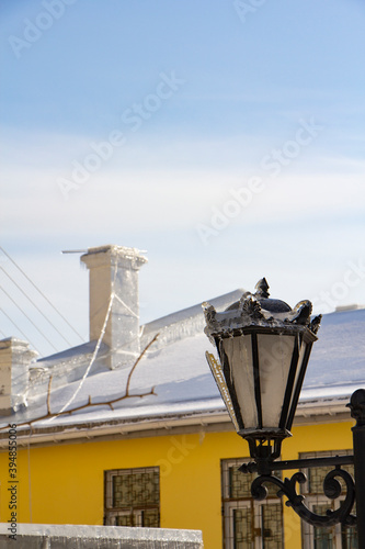 The yellow house and the old street lamp are covered with a thick layer of ice