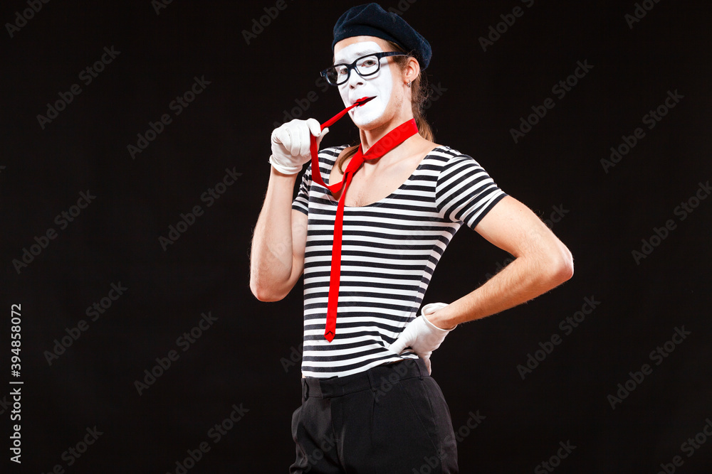 Portrait of male mime artist performing, isolated on black background. Man in beret and striped T-shirt put his red tie in his mouth Portrait of male mime artist performing, isolated on black background. Man in beret and striped T-shirt put his red tie in his mouth