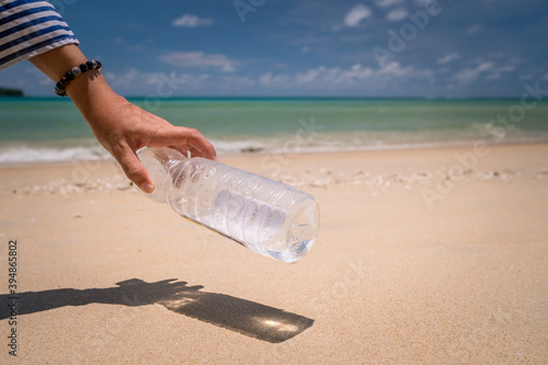 Hand pick up empty water bottle or trash at beautiful beach. Environment Global warming.