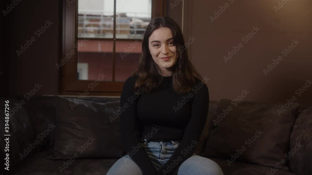 Beautiful dressed girl sitting on sofa looking at camera, smiling and relaxing, home health and comfort concept Beautiful dressed girl sitting on sofa looking at camera, smiling and relaxing, home health and comfort concept