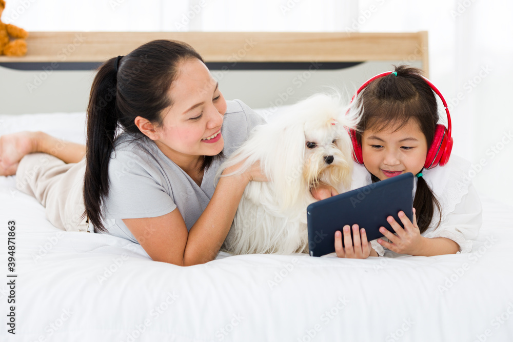 Asian mother and daughter using tablet on bed with dog. Asian mother and daughter using tablet on bed with dog.
