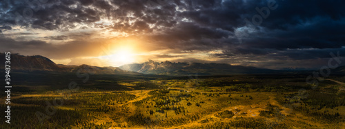 Beautiful Panoramic View of Lush Forests, Trees and Land surrounded by Mountains in Canadian Nature. Dramatic Colorful Sunset Sky. Aerial Drone Shot. Taken near Alaska Highway, Yukon, Canada.