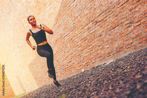 Fit young woman at start running. Runner start a race on a rock track with tall red brick wall as background.