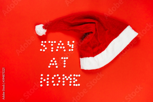 Stay home lettering from round white pills on a red background. Santa hat. High quality photo