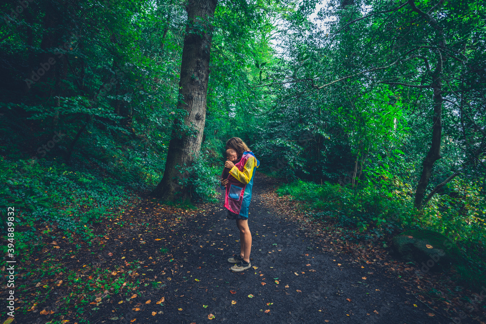 Young mother walking in the forest with her baby in a sling Young mother walking in the forest with her baby in a sling